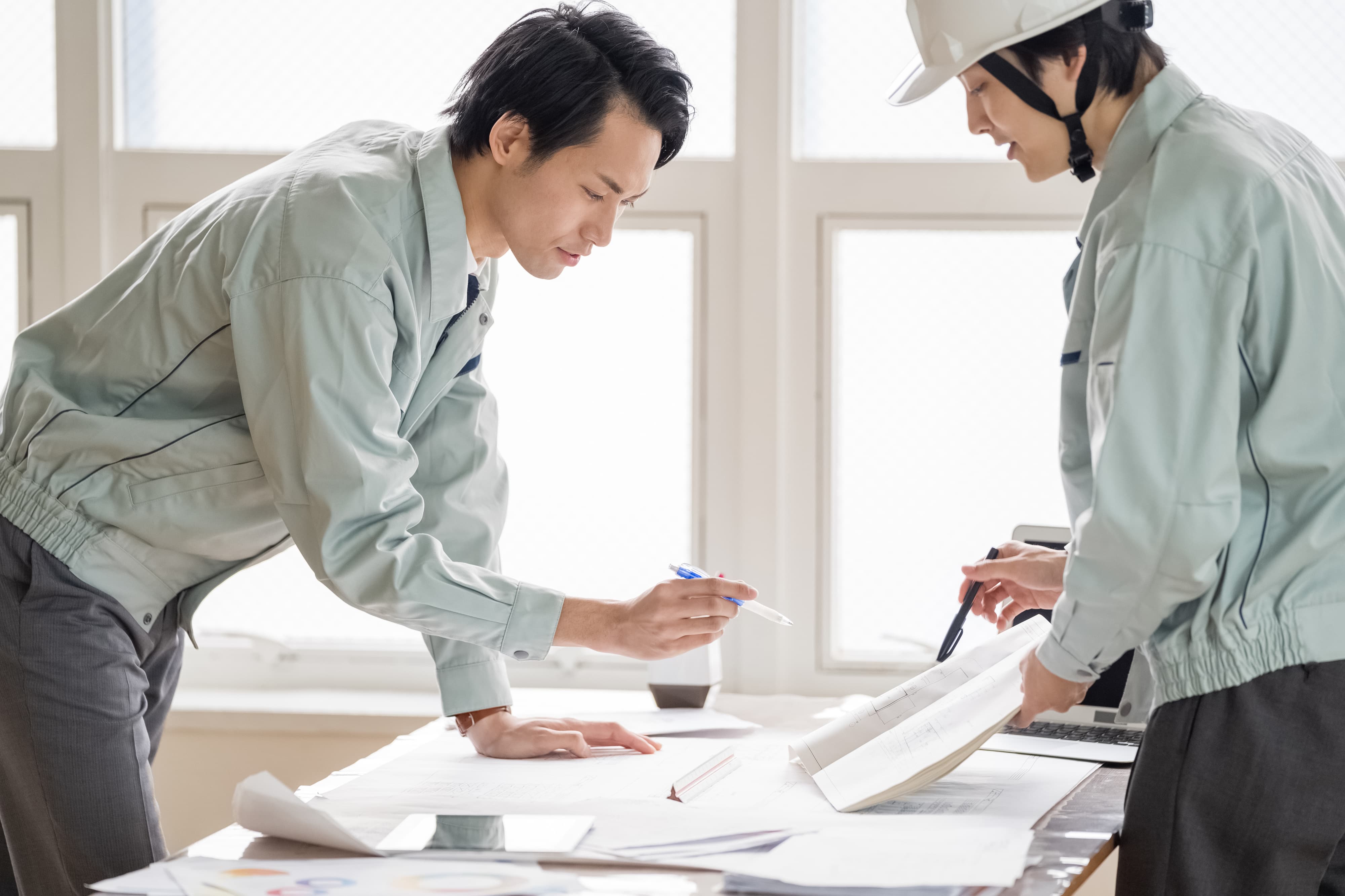 資料や書類を手に話し合う二人の作業着姿の男性